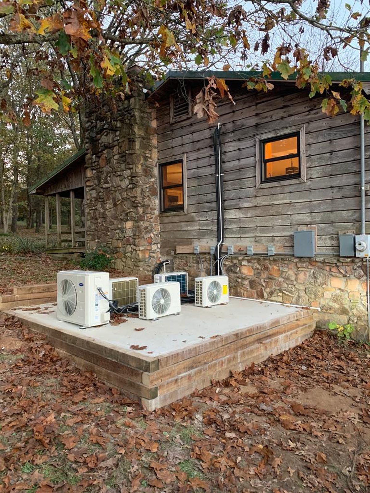 Three ductless mini-split condensing units on a platform outside a rustic cabin
