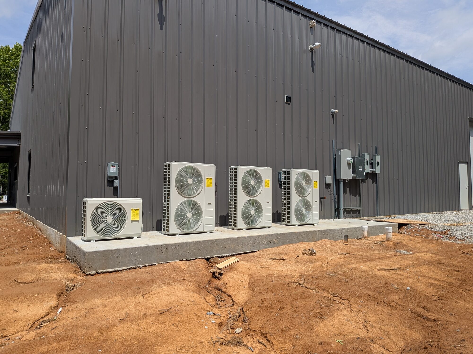 Four Carrier mini-split outdoor units on a concrete pad beside a new metal shop building