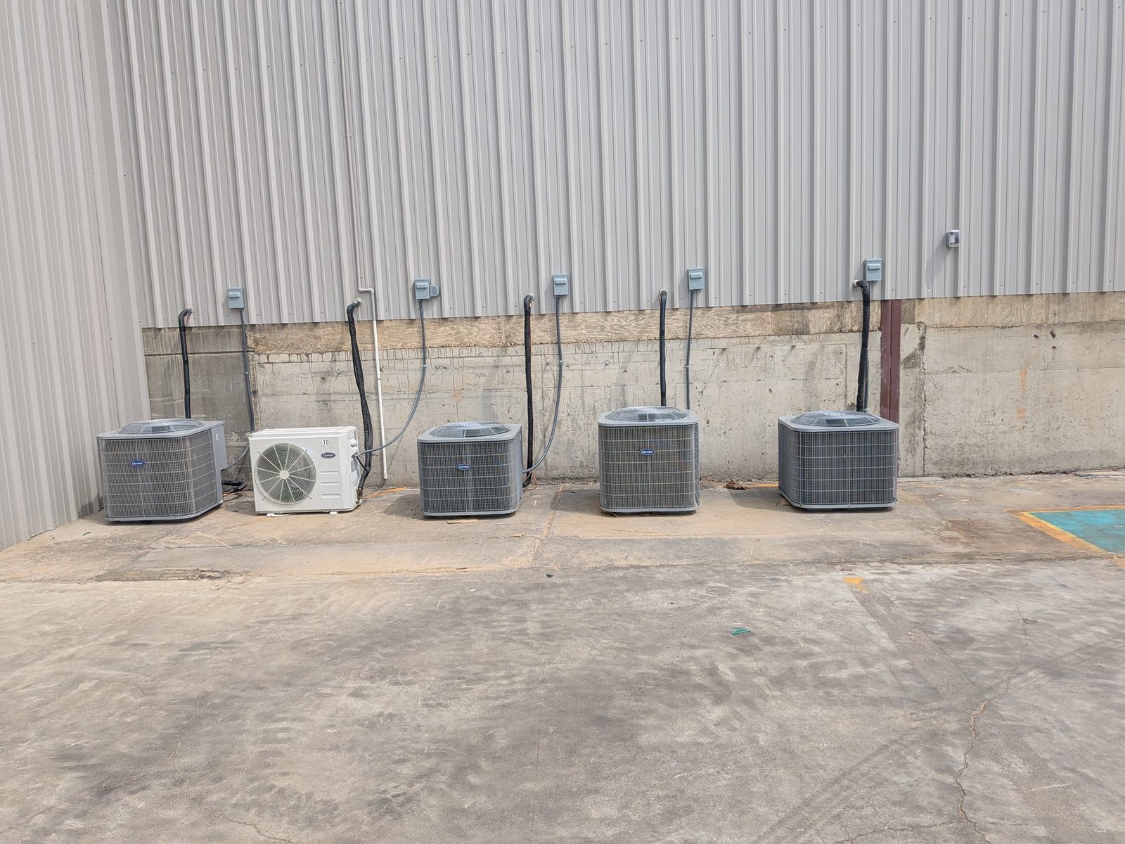 Five separate condensing units, four residential-style Carrier condensers and one mini-split, lined up outside a commercial building